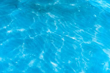 Sahilin arka planında mavi şeffaf deniz suyu. Güneşli bir günde hafif dalgalar ve parıltılarla berrak su yüzeyi