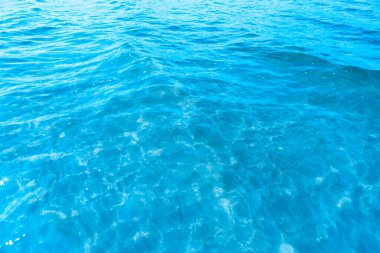 Sahilin arka planında mavi şeffaf deniz suyu. Güneşli bir günde hafif dalgalar ve parıltılarla berrak su yüzeyi