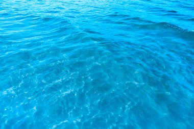 Sahilin arka planında mavi şeffaf deniz suyu. Güneşli bir günde hafif dalgalar ve parıltılarla berrak su yüzeyi