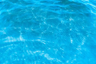 Sahilin arka planında mavi şeffaf deniz suyu. Güneşli bir günde hafif dalgalar ve parıltılarla berrak su yüzeyi