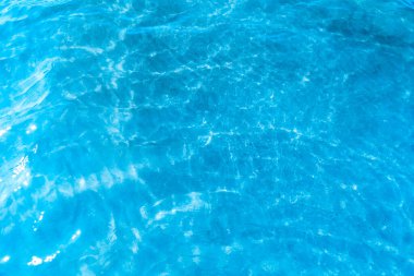 Sahilin arka planında mavi şeffaf deniz suyu. Güneşli bir günde hafif dalgalar ve parıltılarla berrak su yüzeyi