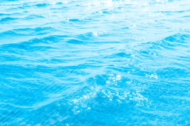 Sahilin arka planında mavi şeffaf deniz suyu. Güneşli bir günde hafif dalgalar ve parıltılarla berrak su yüzeyi