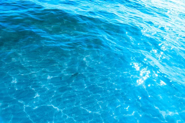 ビーチのテクスチャの背景の近くの青い透明な海の水 晴れた日にはわずかな波とグレアで澄んだ水面 — ストック写真
