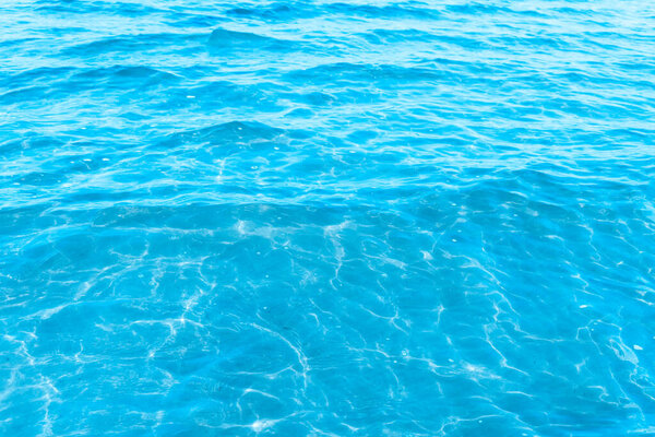 Голубая прозрачная морская вода на фоне текстуры пляжа. чистая поверхность воды с легкими волнами и бликами в солнечный день