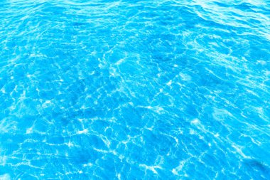 Sahilin arka planında mavi şeffaf deniz suyu. Güneşli bir günde hafif dalgalar ve parıltılarla berrak su yüzeyi