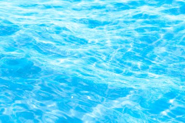 Sahilin arka planında mavi şeffaf deniz suyu. Güneşli bir günde hafif dalgalar ve parıltılarla berrak su yüzeyi