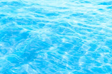 Sahilin arka planında mavi şeffaf deniz suyu. Güneşli bir günde hafif dalgalar ve parıltılarla berrak su yüzeyi