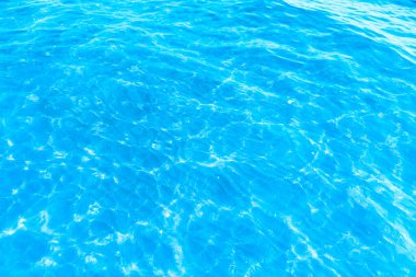 Sahilin arka planında mavi şeffaf deniz suyu. Güneşli bir günde hafif dalgalar ve parıltılarla berrak su yüzeyi