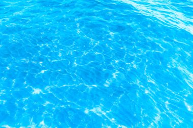 Sahilin arka planında mavi şeffaf deniz suyu. Güneşli bir günde hafif dalgalar ve parıltılarla berrak su yüzeyi