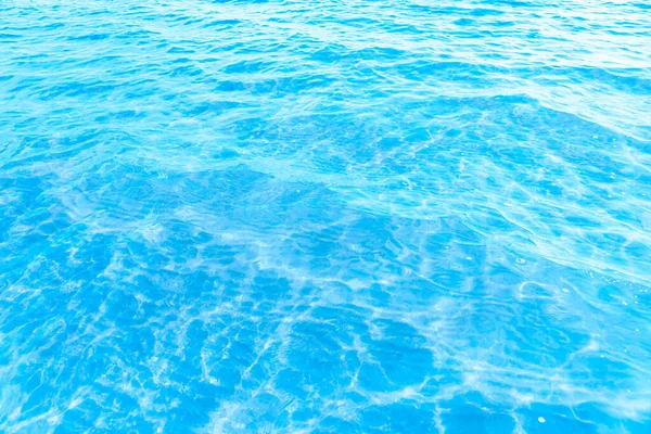 ビーチのテクスチャの背景の近くの青い透明な海の水 晴れた日にはわずかな波とグレアで澄んだ水面 — ストック写真