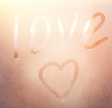 Terli bardağa kazınmış aşk ve kalp. Renkli arka planda sisli cam bir pencereye çizilmiş aşk kalbi. Sisli camda aşkın ve mutluluğun sembolü.