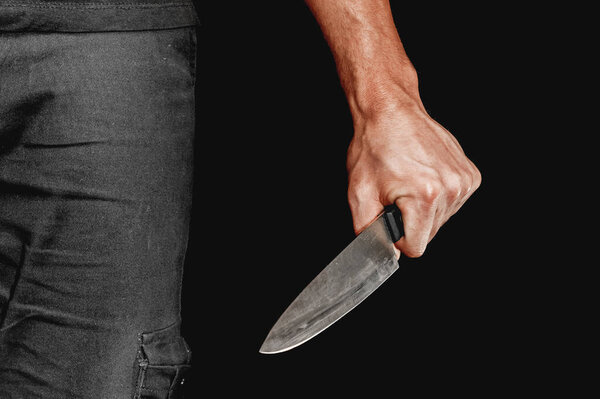 Man's hand holds a knife on black background. topics of violence and murder. thief, killer, rapist, maniac