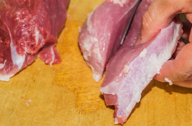 Bir adamın eli kesme tahtasındaki bıçakla taze taze bir eti kesiyor, et kesiyor.