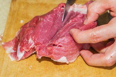 Bir adamın eli kesme tahtasındaki bıçakla taze taze bir eti kesiyor, et kesiyor.