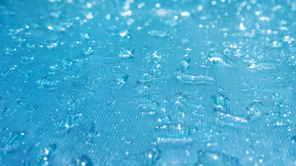 Rain drops on the blue glass bokeh background, shiny raindrops on a glass surface, water drops in a swimming pool closeup