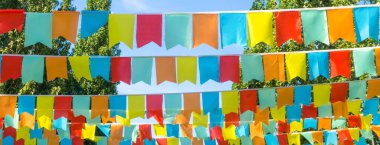Mavi gökyüzüne ve ağaçlara karşı çok renkli bayraklar üçgen şeklinde. Şehir sokak tatili teması için iyi bir geçmiş.