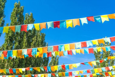 Mavi gökyüzüne ve ağaçlara karşı çok renkli bayraklar üçgen şeklinde. Şehir sokak tatili teması için iyi bir geçmiş.