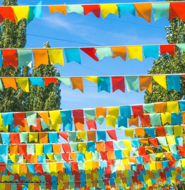 Mavi gökyüzüne ve ağaçlara karşı çok renkli bayraklar üçgen şeklinde. Şehir sokak tatili teması için iyi bir geçmiş.