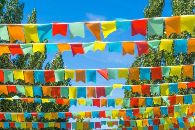 Mavi gökyüzüne ve ağaçlara karşı çok renkli bayraklar üçgen şeklinde. Şehir sokak tatili teması için iyi bir geçmiş.