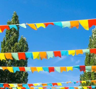 Mavi gökyüzüne ve ağaçlara karşı çok renkli bayraklar üçgen şeklinde. Şehir sokak tatili teması için iyi bir geçmiş.