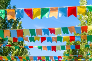 Mavi gökyüzüne ve ağaçlara karşı çok renkli bayraklar üçgen şeklinde. Şehir sokak tatili teması için iyi bir geçmiş.