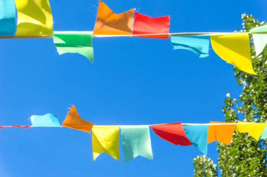 Mavi gökyüzüne ve ağaçlara karşı çok renkli bayraklar üçgen şeklinde. Şehir sokak tatili teması için iyi bir geçmiş.