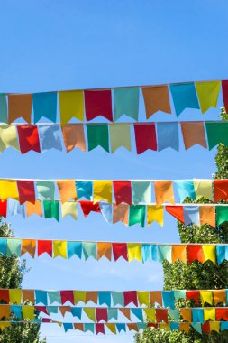 Mavi gökyüzüne ve ağaçlara karşı çok renkli bayraklar üçgen şeklinde. Şehir sokak tatili teması için iyi bir geçmiş.