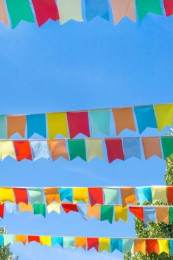 Mavi gökyüzüne ve ağaçlara karşı çok renkli bayraklar üçgen şeklinde. Şehir sokak tatili teması için iyi bir geçmiş.
