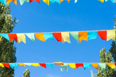 Mavi gökyüzüne ve ağaçlara karşı çok renkli bayraklar üçgen şeklinde. Şehir sokak tatili teması için iyi bir geçmiş.