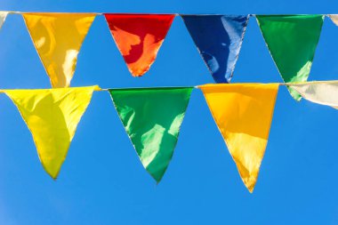Çok renkli bayraklar mavi gökyüzüne karşı üçgen şeklinde şekillenir. Şehir sokak tatili teması için iyi bir geçmiş.