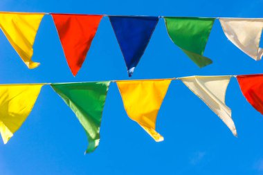 Çok renkli bayraklar mavi gökyüzüne karşı üçgen şeklinde şekillenir. Şehir sokak tatili teması için iyi bir geçmiş.