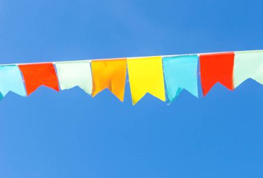 Çok renkli bayraklar mavi gökyüzüne karşı üçgen şeklinde şekillenir. Şehir sokak tatili teması için iyi bir geçmiş.