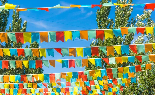 Mavi gökyüzüne ve ağaçlara karşı çok renkli bayraklar üçgen şeklinde. Şehir sokak tatili teması için iyi bir geçmiş.