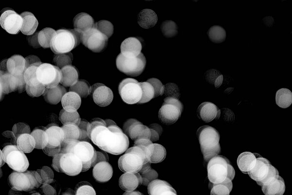 White bokeh on a black background closeup, bright glare of light texture, light lights, black and white photo