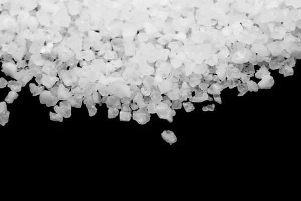 Spilled white sea salt on a black background. Transparent pebbles on a black background