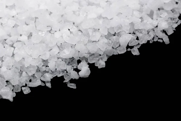 Spilled white sea salt on a black background. Transparent pebbles on a black background