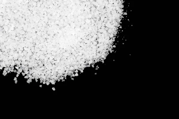 Spilled white sea salt on a black background. Transparent pebbles on a black background