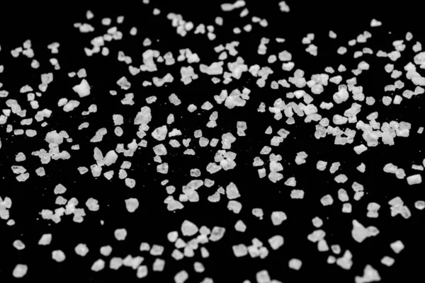 Spilled white sea salt on a black background. Transparent pebbles on a black background