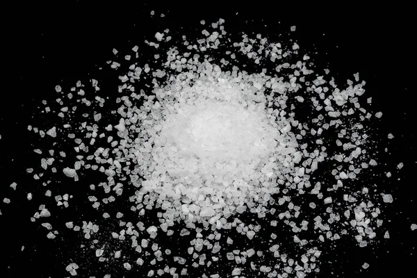 Spilled white sea salt on a black background. Transparent pebbles on a black background