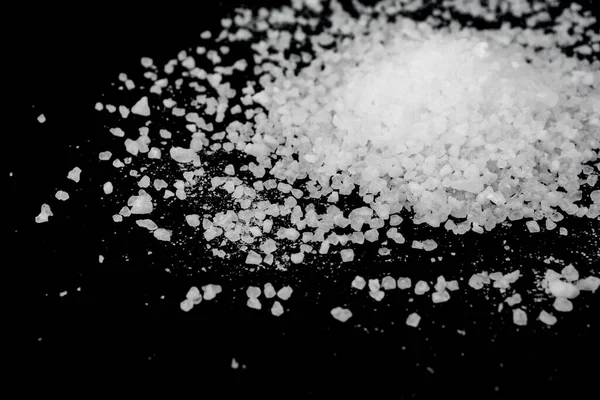 Spilled white sea salt on a black background. Transparent pebbles on a black background