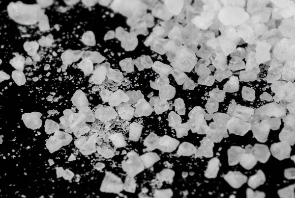 Spilled white sea salt on a black background. Transparent pebbles on a black background