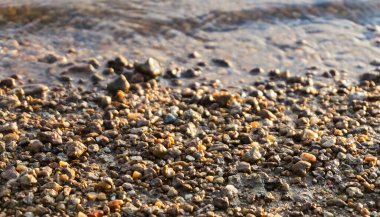 Güneşin doğuşunda taşlı plaj, günbatımı kumsalında çakıl taşı, deniz dalgası ve çakıl taşı kıyısı yakın çekim