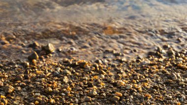 Güneşin doğuşunda taşlı plaj, günbatımı kumsalında çakıl taşı, deniz dalgası ve çakıl taşı kıyısı yakın çekim