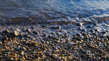 Güneşin doğuşunda taşlı plaj, günbatımı kumsalında çakıl taşı, deniz dalgası ve çakıl taşı kıyısı yakın çekim