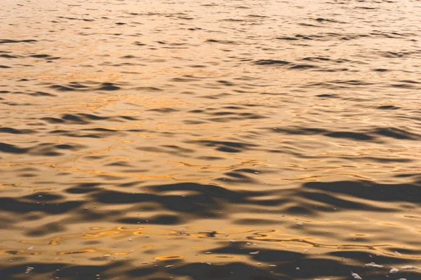 Surface of water with waves background texture, wave close up, light playing on the sea surface, the surface of golden water at sunset or dawn, orange yellow scarlet rose water, sunrise, sunset a sea