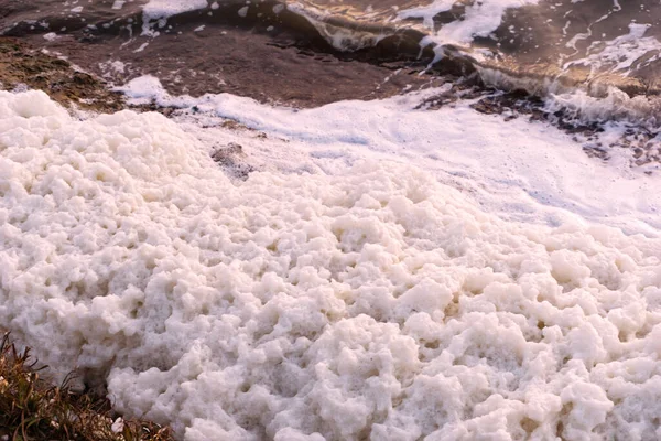 White foam accumulations on the shore near the water surface texture background, foam aggregates, scum, river froth, cumulus foam, airy foam, scarlet peach beige pink sea lake foam,