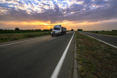 Kırsal bir yolda gün batımında dramatik bir geçmişi olan büyük bir kamyon.. 