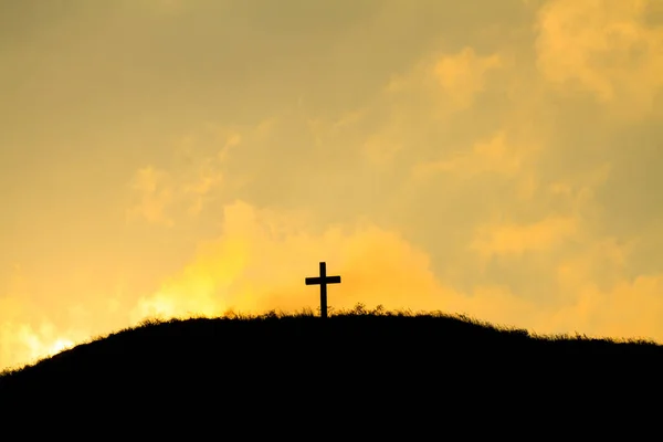 Religious cross silhouette with yellow-orange sky sunset background.