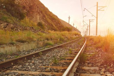 Gün batımında etrafında yeşil çimenler ve dağlar olan tren istasyonu.. 