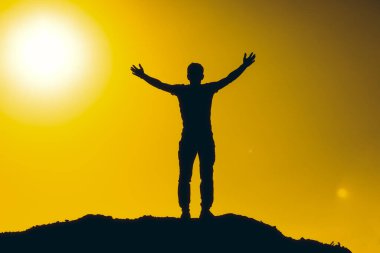 Rahatlamış adamın silueti gün batımının keyfini çıkarıyor, ellerini havaya kaldırıyor. Seyahat ve tatil kavramı.